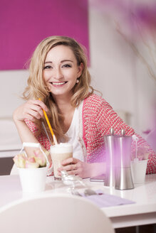 Glückliche blonde Frau sitzt in einem Café mit Latte Macciato - JUNF000289