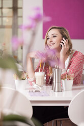 Smiling blond woman sitting in a coffee with glass of Latte Macchiato telephoning - JUNF000290