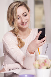 Portrait of smiling blond woman sitting in a coffee shop using smartphone - JUNF000276