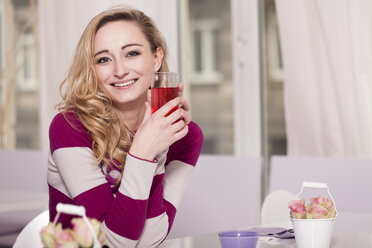 Lächelnde blonde Frau, die in einem Café sitzt und ein Getränk hält - JUNF000280