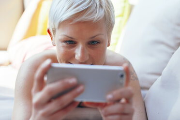 Junge Frau liegt auf einer Couch auf ihrer Terrasse und benutzt ihr Smartphone - EBSF000476