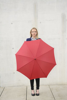 Businesswoman with red umbrella in front of concrete wall - BFRF001027