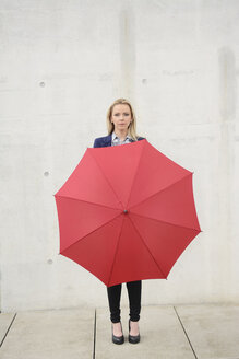 Geschäftsfrau mit rotem Regenschirm vor einer Betonwand - BFRF001027