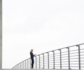 Businesswoman with digital tablet in front of railing - BFRF001059