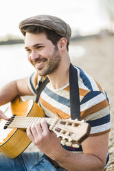 Mann sitzt am Flussufer und spielt Gitarre - UUF003744