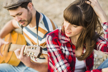 Pärchen sitzt am Flussufer und spielt Gitarre - UUF003745