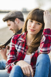 Pärchen sitzt am Flussufer und spielt Gitarre - UUF003747