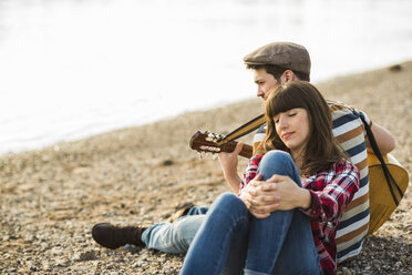 Couple sitting by the riverside, playing guitar - UUF003748