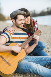 Pärchen sitzt am Flussufer und spielt Gitarre - UUF003751