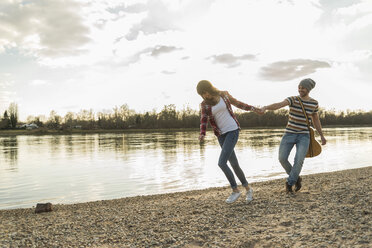 Glückliches junges Paar am Flussufer, das Hand in Hand spazieren geht - UUF003754