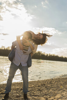 Glückliches junges Paar, das sich am Ufer des Flusses amüsiert - UUF003759