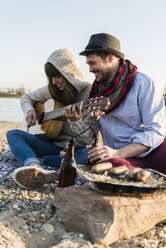 Couple sitting by the riverside, playing guitar - UUF003768