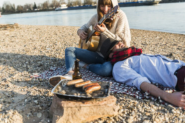 Pärchen sitzt am Flussufer und spielt Gitarre - UUF003769