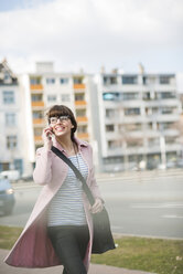 Junge Frau geht auf der Straße und benutzt ein Mobiltelefon - UUF003787