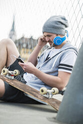 Junger Mann mit Skateboard hört Musik vom Smartphone - UUF003857
