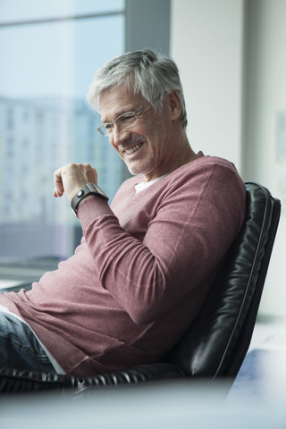 Lächelnder Mann mit Smartwatch in einem Ledersessel sitzend, lizenzfreies Stockfoto