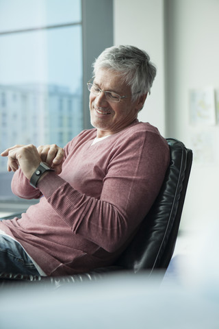 Smiling man sitting in a leather chair using smartwatch stock photo