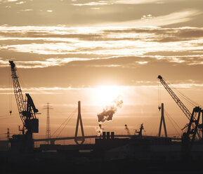 Germany, Hamburg, Silhouettes of harbour cranes at sunset, Koehlbrand bridge in the background - KRPF001409