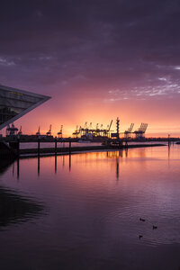 Deutschland, Hamburg, Altona, Bürogebäude Dockland bei Sonnenuntergang, Hamburger Hafen mit Hafenkränen im Hintergrund - KRPF001420