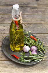 Rosmarinöl in der Flasche, Knoblauch, Rosmarin und Chilischoten auf dem Teller - SARF001599