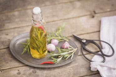 Rosmarinöl in Flasche, Knoblauch, Rosmarin und Chilischoten auf Teller, Schere und Küchentuch auf Holz - SARF001601