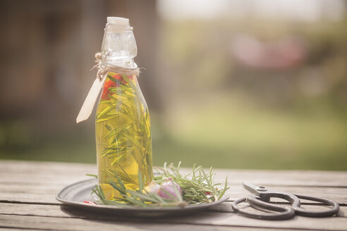 Rosmarinöl in Flasche, Knoblauch, Rosmarin auf Teller, Schere auf Holz - SARF001602