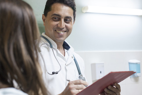 Lächelnder Arzt, der sich Notizen macht und dem Patienten zuhört, lizenzfreies Stockfoto