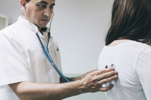 Arzt hört den Rücken eines Patienten mit Stethoskop ab, lizenzfreies Stockfoto