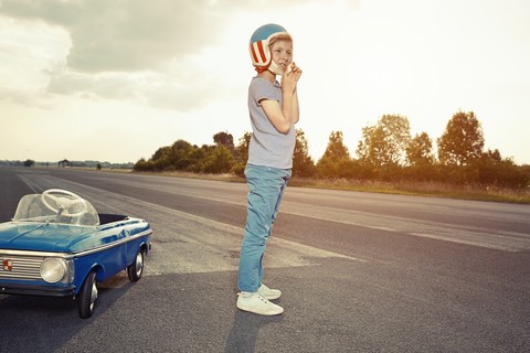 Junge steht neben einem Tretauto auf der Rennstrecke, lizenzfreies Stockfoto