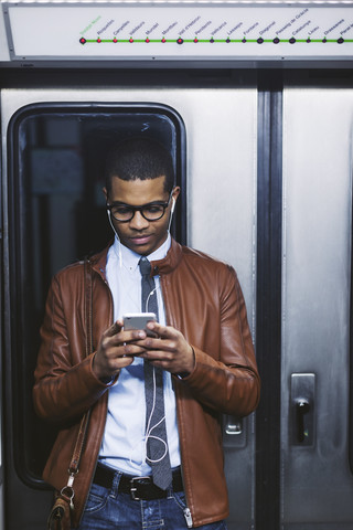 Spanien, Barcelona, Geschäftsmann mit Smartphone und Kopfhörern hört Musik in der U-Bahn, lizenzfreies Stockfoto