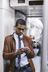 Businessman with smartphone and earphones hearing music on the subway train - EBSF000489