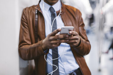 Businessman with smartphone and earphones hearing music on the subway train - EBSF000490