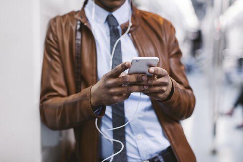 Geschäftsmann mit Smartphone und Kopfhörern hört Musik in der U-Bahn - EBSF000490