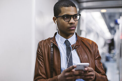 Porträt eines Geschäftsmannes mit Smartphone und Kopfhörern, der in der U-Bahn Musik hört - EBSF000491