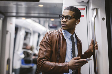 Geschäftsmann mit Smartphone und Kopfhörern hört Musik in der U-Bahn - EBSF000493