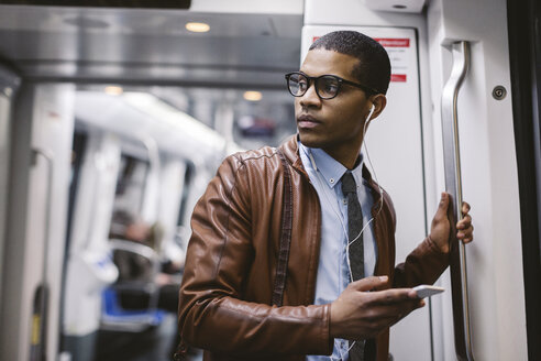 Geschäftsmann mit Smartphone und Kopfhörern hört Musik in der U-Bahn - EBSF000493