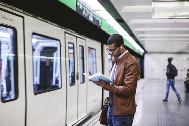 Spain, Barcelona, businessman standing at underground station platform reading book - EBSF000500