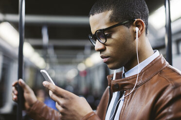 Porträt eines Geschäftsmannes mit Smartphone und Kopfhörern, der in der U-Bahn Musik hört - EBSF000506