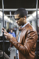 Porträt eines Geschäftsmannes mit Smartphone und Kopfhörern, der in der U-Bahn Musik hört - EBSF000507