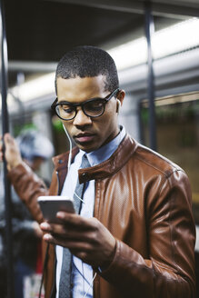 Porträt eines Geschäftsmannes mit Smartphone und Kopfhörern, der in der U-Bahn Musik hört - EBSF000508