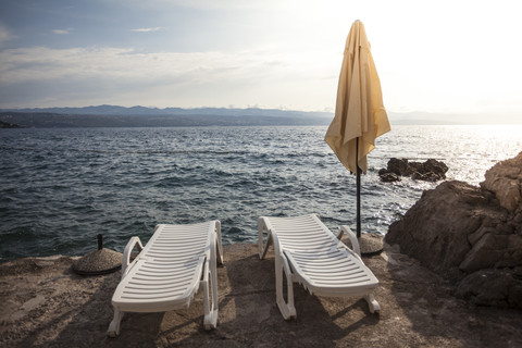 Kroatien, Blick auf das Adriatische Meer mit zwei Liegestühlen und einem Sonnenschirm im Vordergrund, lizenzfreies Stockfoto