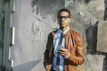 Porträt eines Geschäftsmannes mit Smartphone, Lederjacke und Brille - EBSF000513