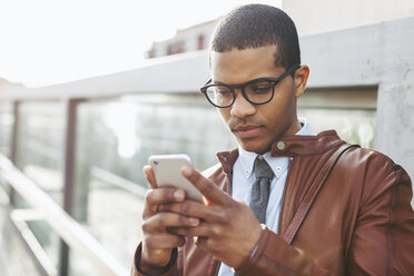 Portrait of businessman with smartphone wearing leather jacket and glasses - EBSF000517