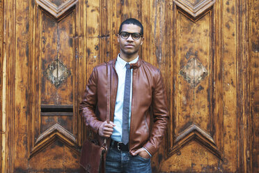 Porträt eines Geschäftsmannes mit Lederjacke und Brille vor einer Holztür - EBSF000529