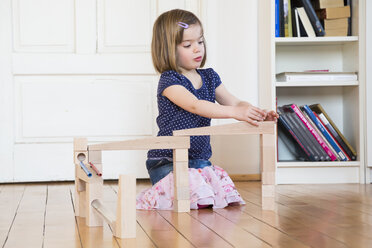 Kleines Mädchen hockt auf dem Boden und spielt mit einer Murmelbahn - LVF003162