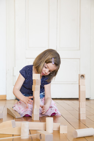 Kleines Mädchen hockt auf dem Boden und spielt mit hölzernen Bauklötzen, lizenzfreies Stockfoto