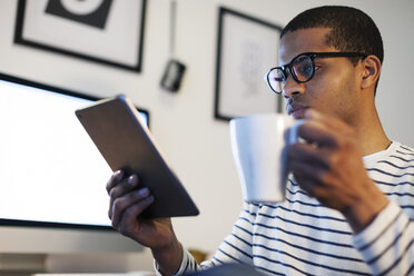 Junger kreativer Mann mit Mini-Tablet in der Kaffeepause in seinem Heimbüro - EBSF000558