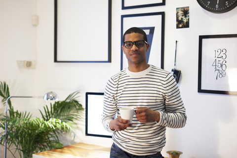 Junger kreativer Mann macht Kaffeepause in seinem Büro zu Hause, lizenzfreies Stockfoto