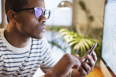 Junger kreativer Mann mit Smartphone in seinem Heimbüro - EBSF000556