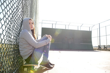 Traurige Frau sitzt auf ihrem Skateboard auf einem Sportplatz - BFRF001068